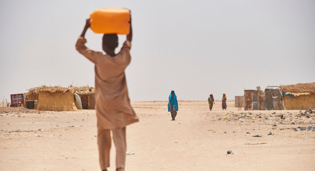 Gutt bærer en vannkanne på hodet gjennom en flyktningleir nord i Nigeria