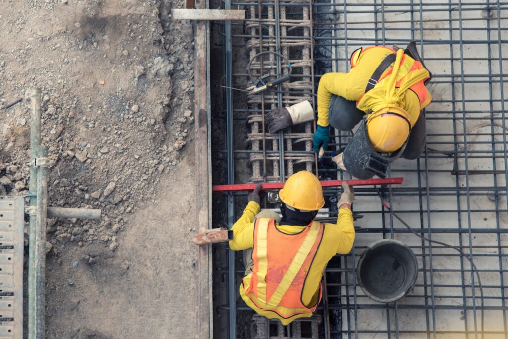 To arbeidere i gult verneutstyr jobber på en byggeplass