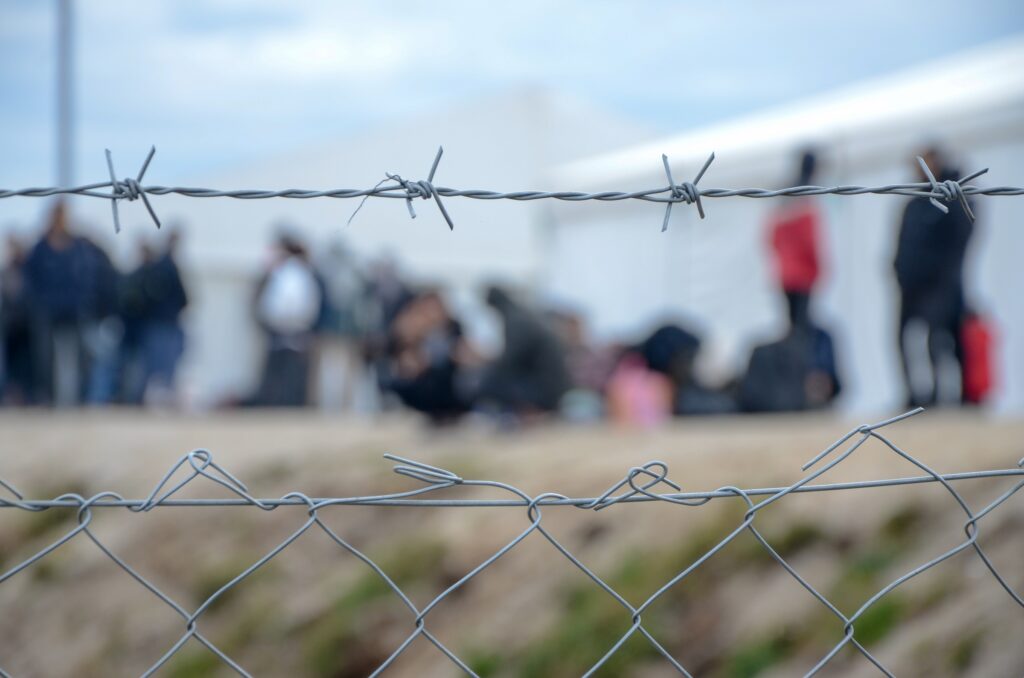 En gruppe migranter skimtes bak et piggtrådgjerde