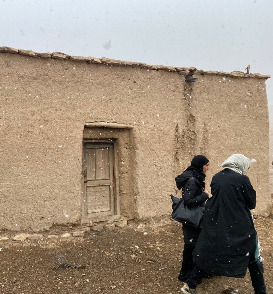 To kvinner går med et afghansk hus i bakgrunnen.