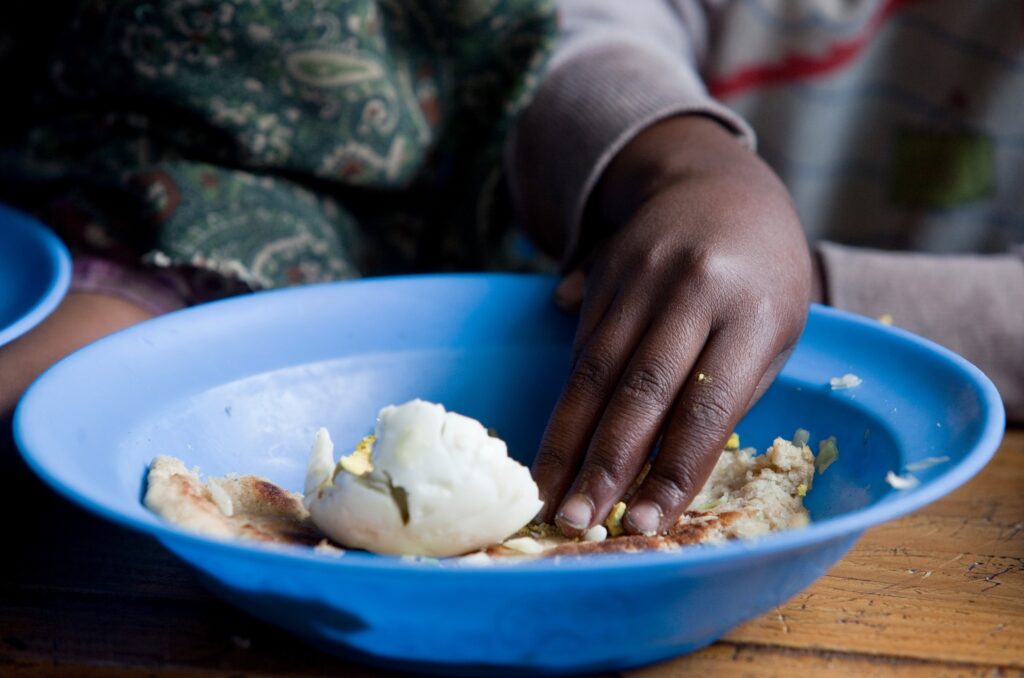 Barnehånd som samler opp mat fra en dyp tallerken. 