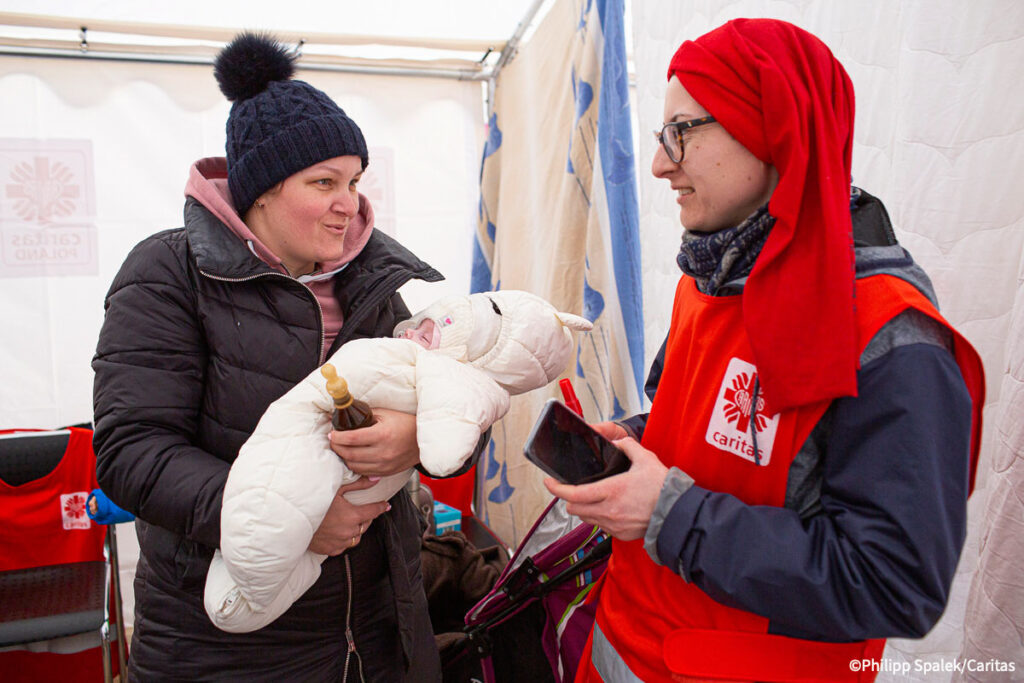 Ukrainsk kvinnelig flyktning holder babyen sin, mens hun snakker med en av Caritas Polens hjelpearbeidere i mottaksteltet på grensen.