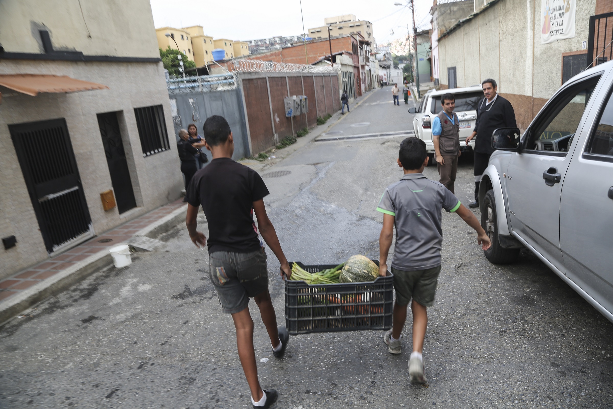 To gutter bærer en kasse med grønnsaker nedover en gate i Venezuela