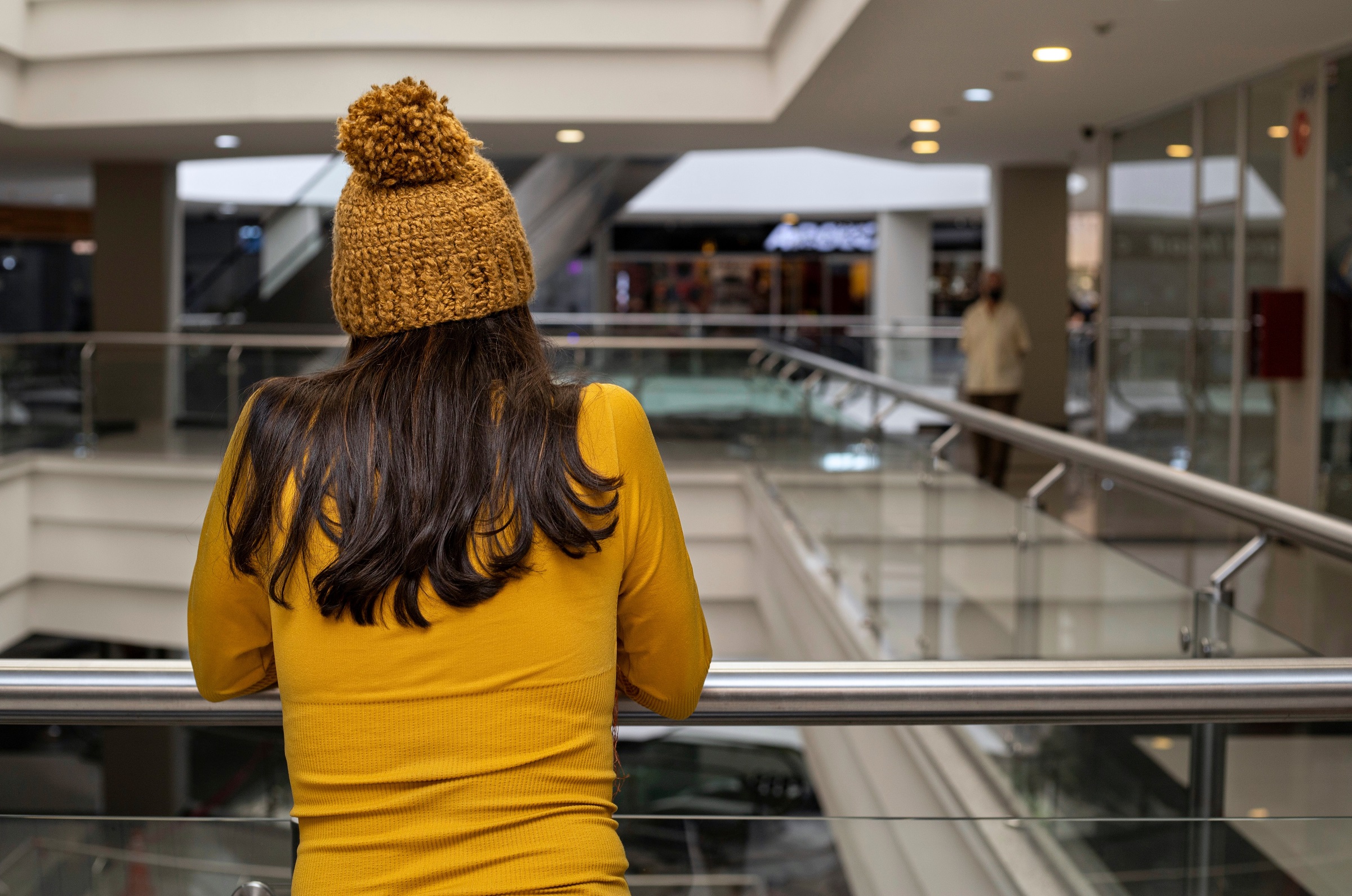 Kvinne med gul genser og gul lue står med ryggen til inne på et kjøpesenter.