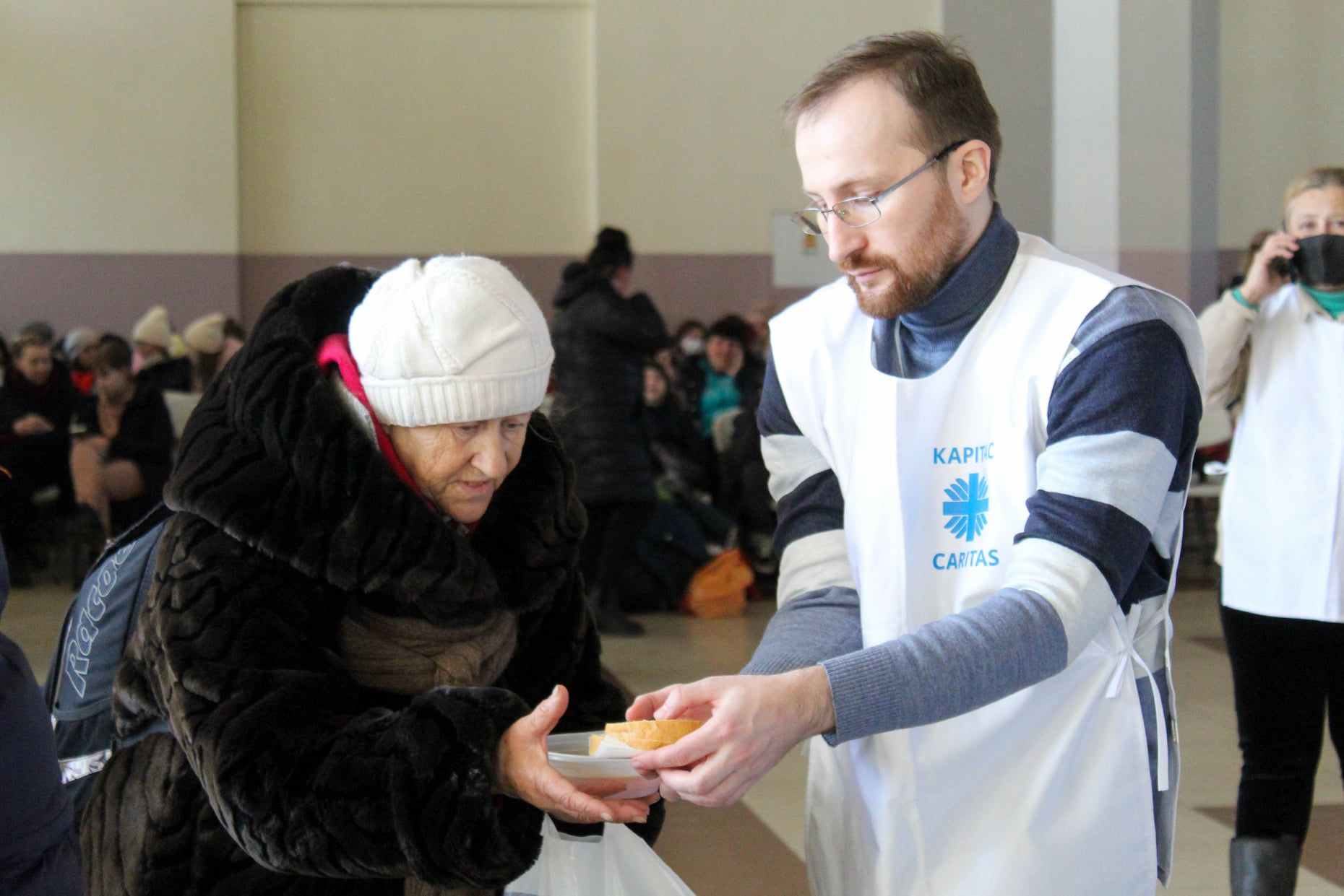 Starsza kobieta otrzymuje kromkę chleba od wolontariusza w Caritas Ukraina.