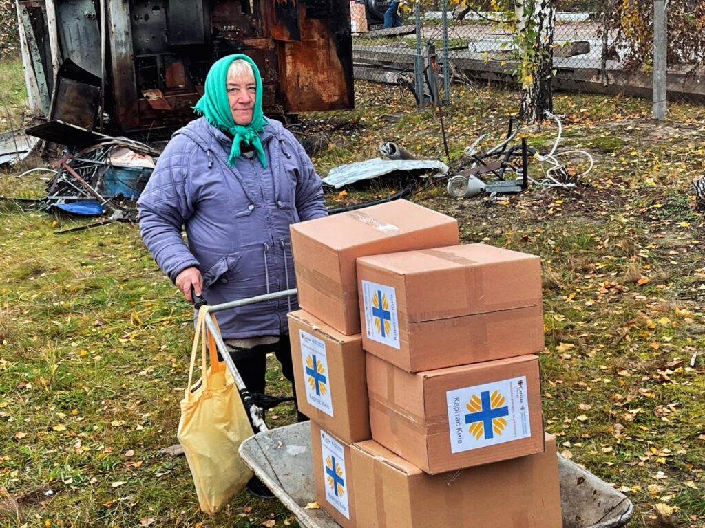 En eldre kvinne triller bort kasser med mat og annet utstyr som er finansiert med støtte fra Caritas Norge.