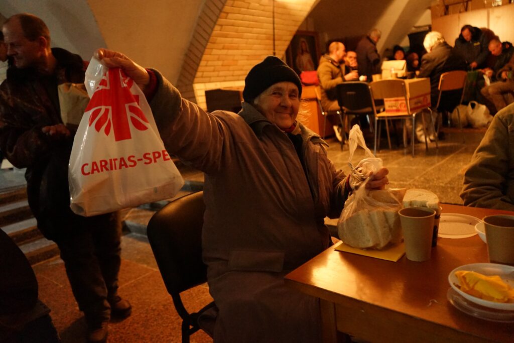 En eldre ukrainsk kvinne smiler mens hun viser frem en pose  med mat hun har fått fra hjelpeorganisasjonen Caritas