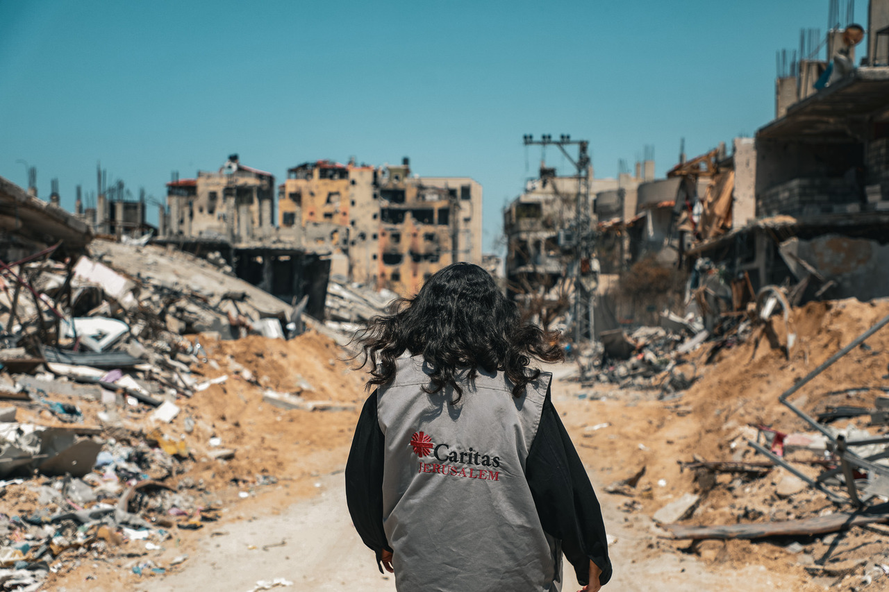 Caritas-Gaza employee walks on a dirt road surrounded by ruins
