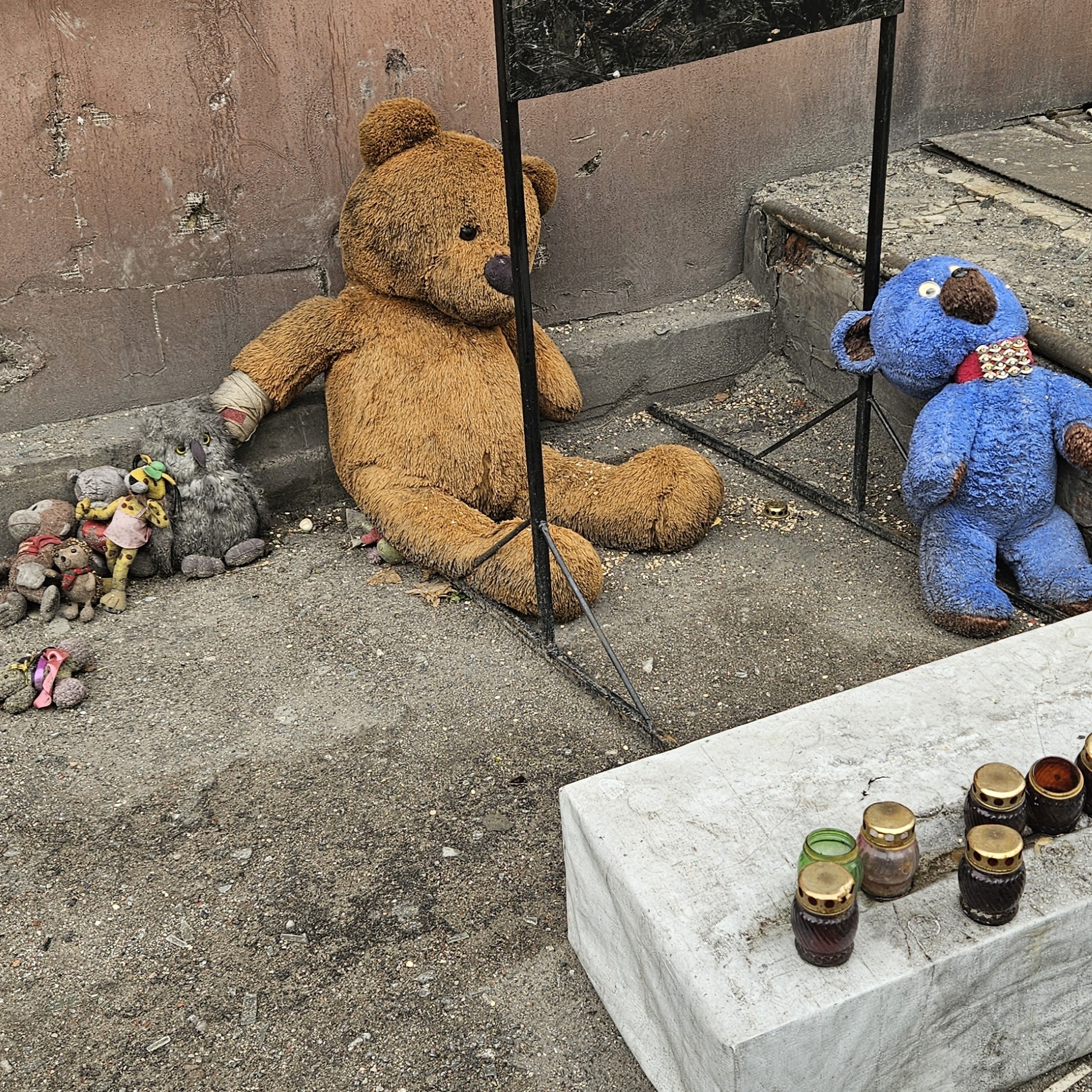 Two tired teddy bears and grave lanterns outside a house in Eastern Ukraine