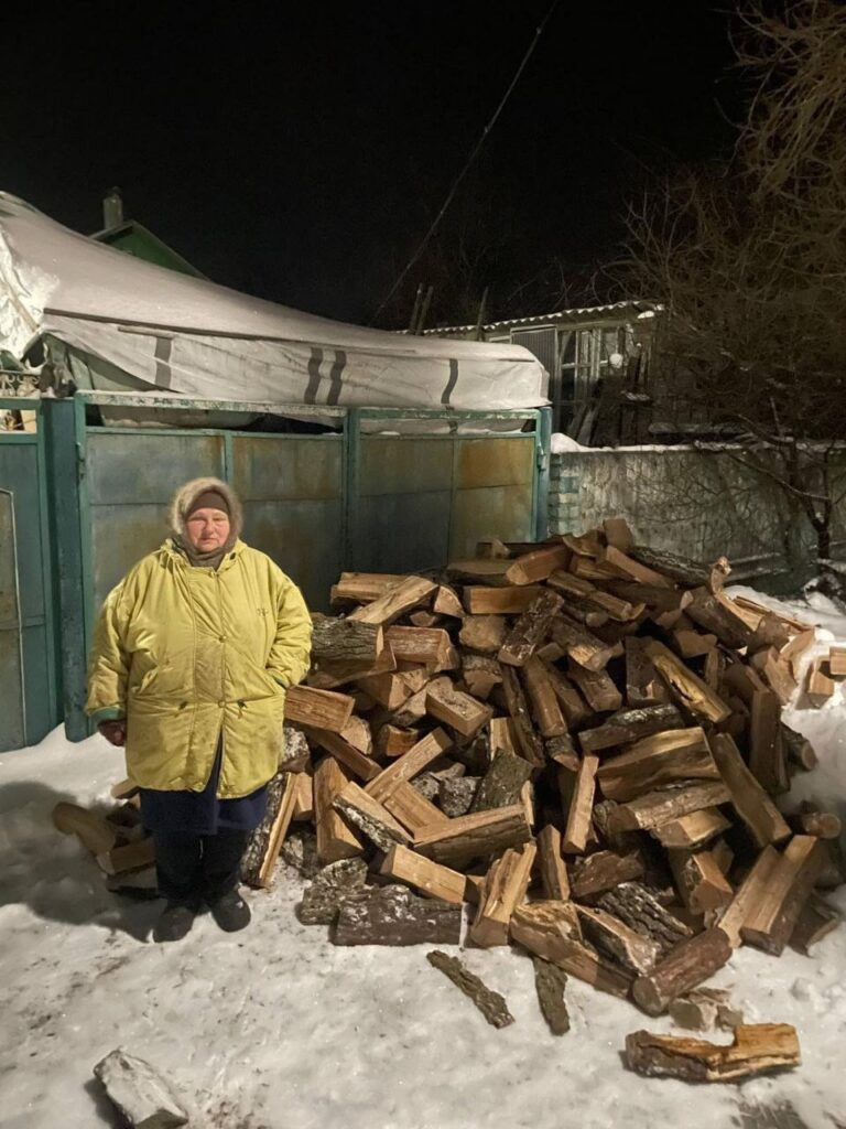 Eldre dame i Øst-Ukraina står ved siden av veden hun har fått av Caritas til å fyre med.