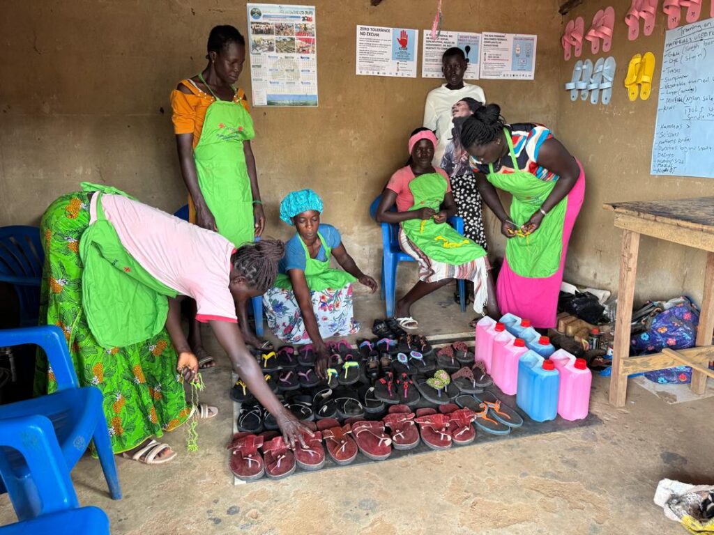 En gruppe med kvinner i Bidibidi, Uganda, viser fram egenproduserte sko og såpe