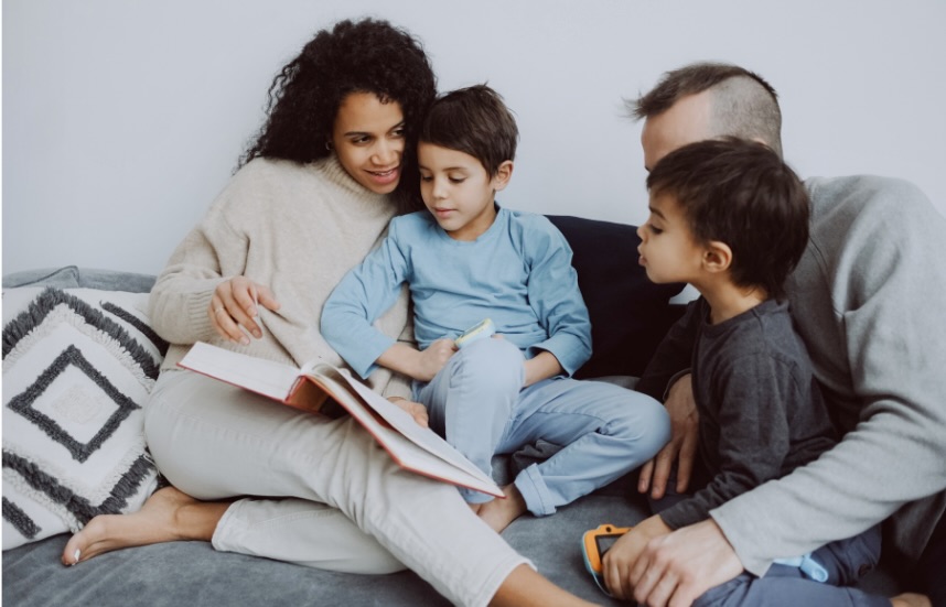 Familie; mor, far og to sønner samlet i sofaen omkring en bok.